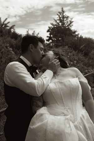 Black and white photo of a bride and groom sharing a romantic kiss outdoors on their wedding day.