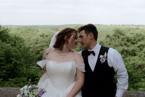 Bride and groom share a romantic moment outdoors, surrounded by lush greenery, in wedding attire with a floral boutonniere.