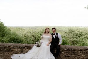 Bride and groom posing together on a stone wall overlooking a lush green landscape on their wedding day.