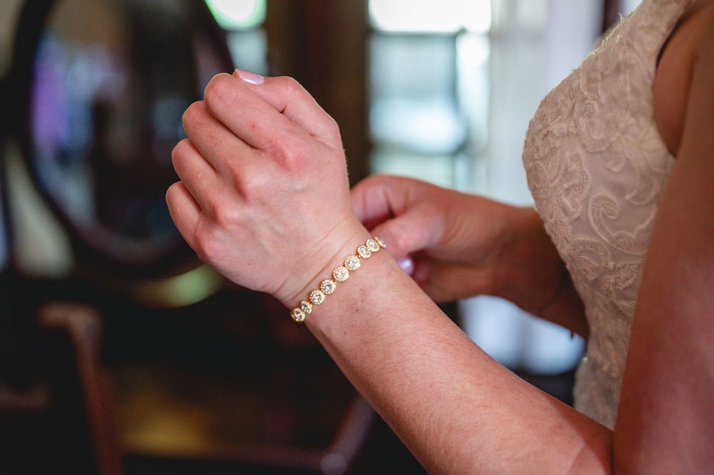 Bride having a gold bracelet fastened on her wrist by a bridesmaid before the wedding ceremony.