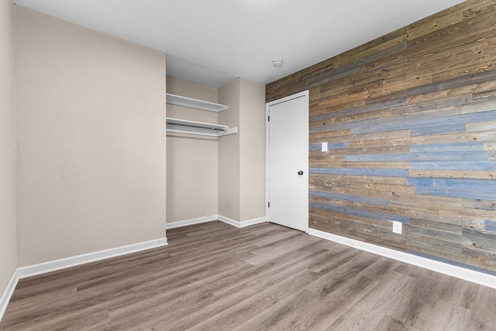 Bedroom with reclaimed wood accent wall, open closet shelving, and hardwood floors.