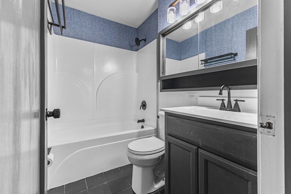 Bathroom with tub-shower combo, dark vanity, toilet, and blue tile walls.