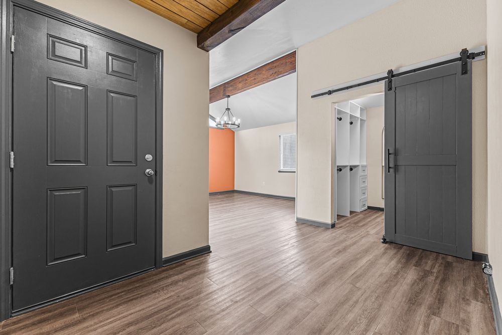 Entryway featuring a dark front door, barn door, wood beam ceiling, and hardwood-style flooring.