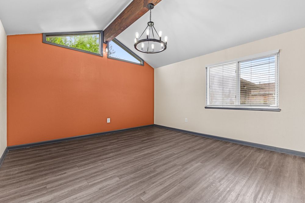 Vaulted room with orange accent wall, dark hardwood floors, exposed wood beam, and chandelier lighting.