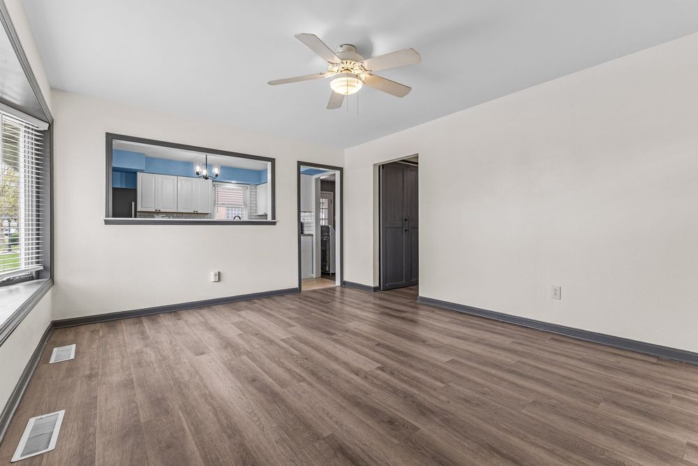 Empty living room with hardwood floors, ceiling fan, and pass-through window to kitchen.