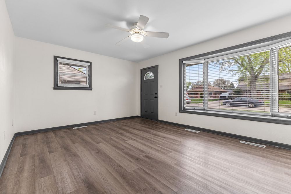 Bright living room with dark hardwood floors, ceiling fan, large window, and neutral walls in a modern home.