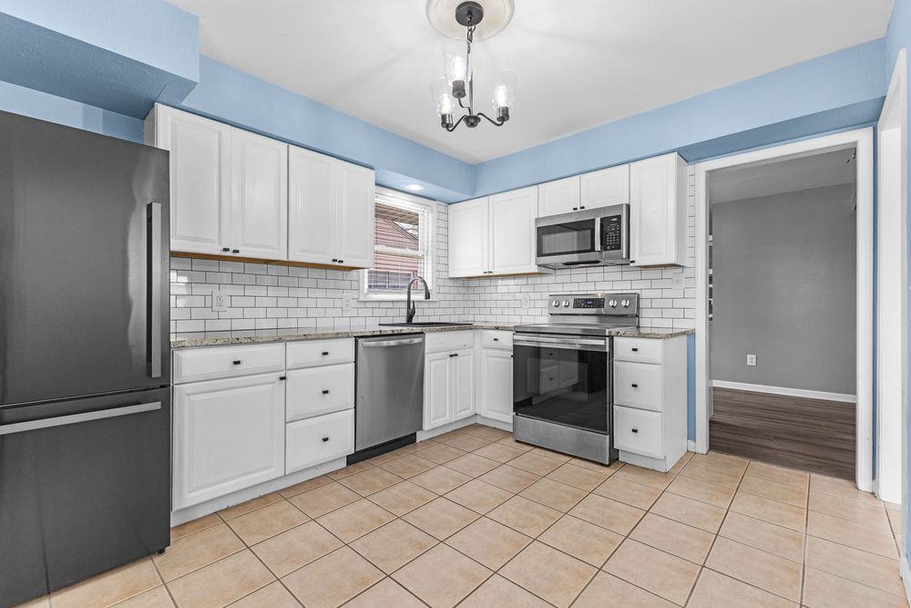 Modern kitchen with white cabinets, stainless steel appliances, subway tile backsplash, and tile floors.