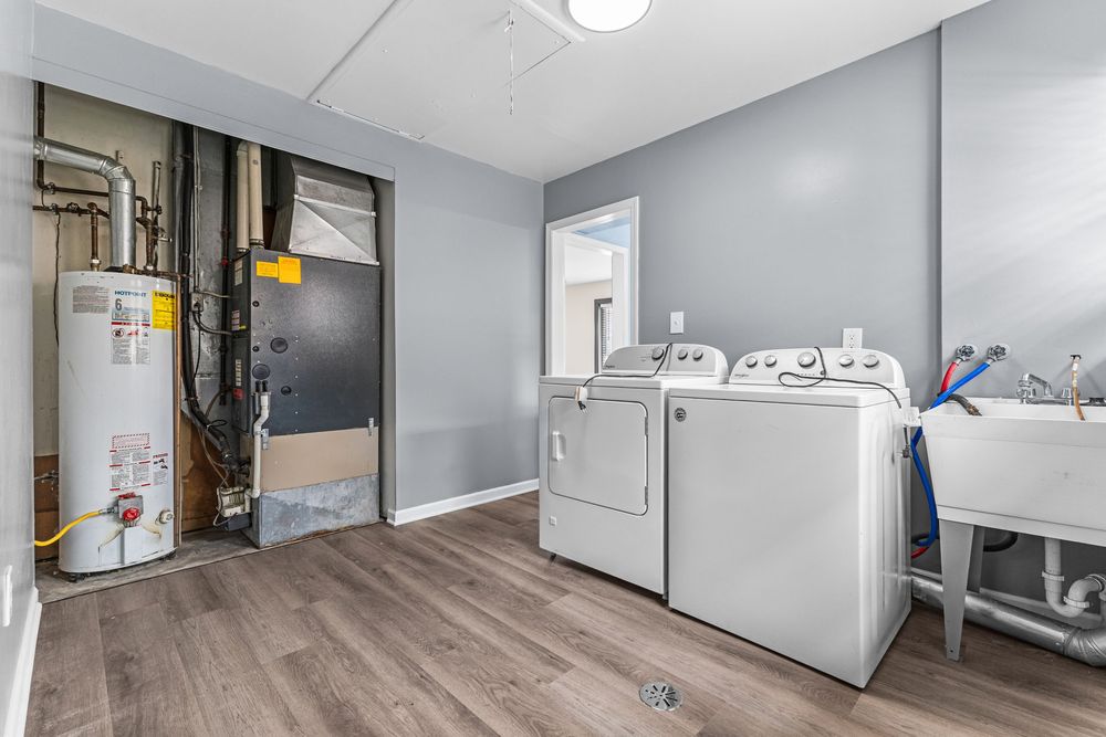 Laundry room with washer and dryer, water heater, hardwood floors, and utility sink.