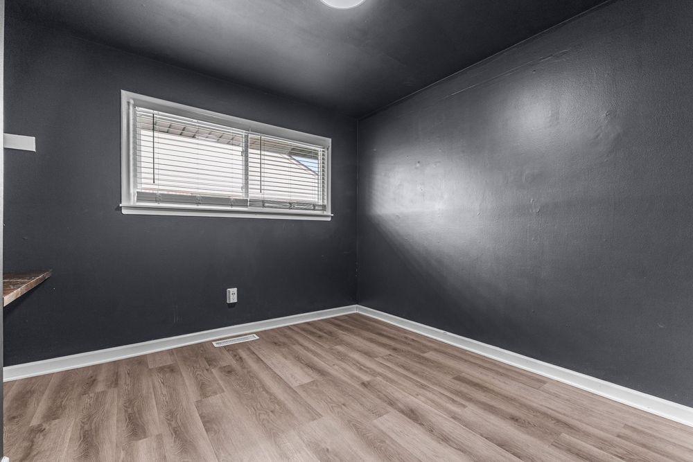 Empty room with dark gray walls, white baseboards, a window with blinds, and light wood laminate flooring.