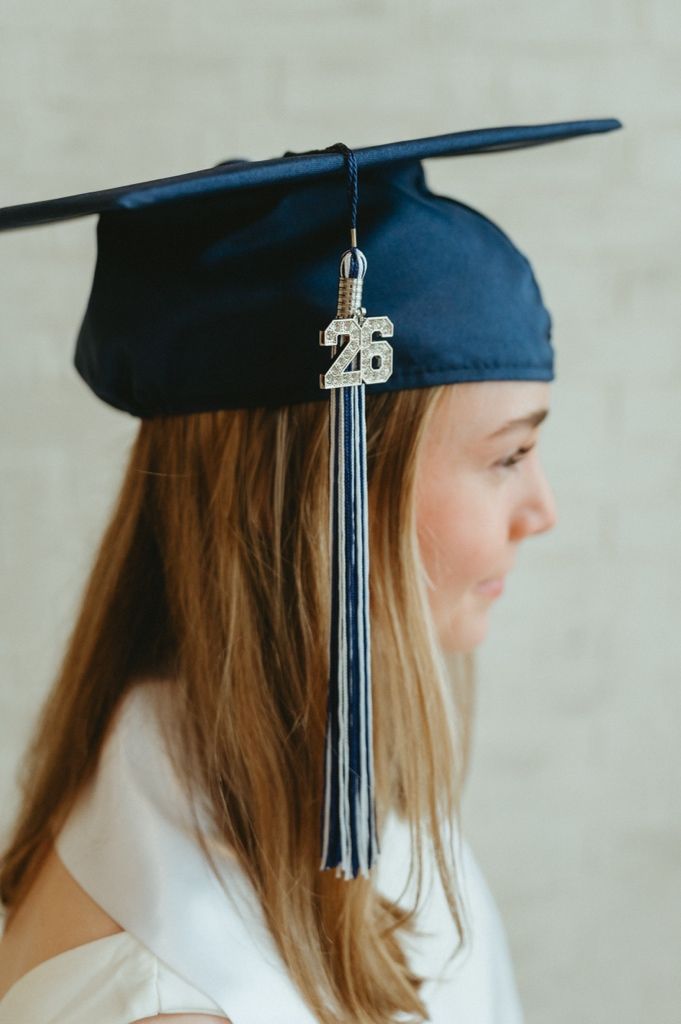 Side profile of graduate wearing navy mortarboard cap with silver 26 tassel charm in long blonde hair.