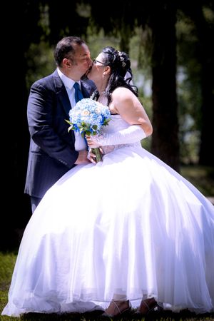 Bride and groom share a romantic kiss outdoors, bride holding a blue hydrangea bouquet in white gown.