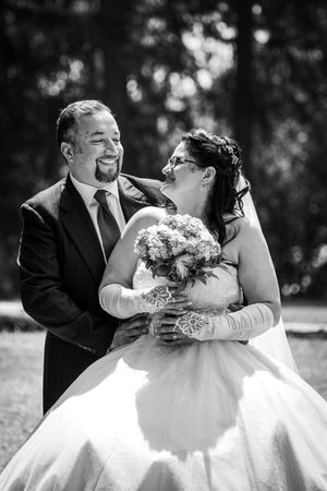 Black and white photo of a smiling bride and groom sharing a joyful moment outdoors on their wedding day.