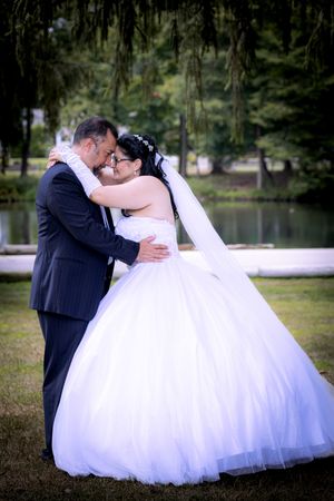 Bride and groom embrace tenderly in a white ballgown wedding dress and navy suit by a serene pond.