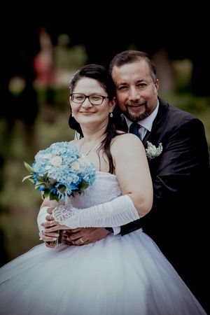 Groom embraces bride in white tulle gown as she holds a blue hydrangea bouquet outdoors.