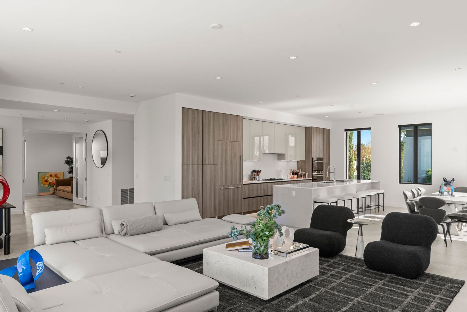 Modern open-plan living room with grey sectional sofa, white coffee table, and sleek kitchen with bar seating in background.