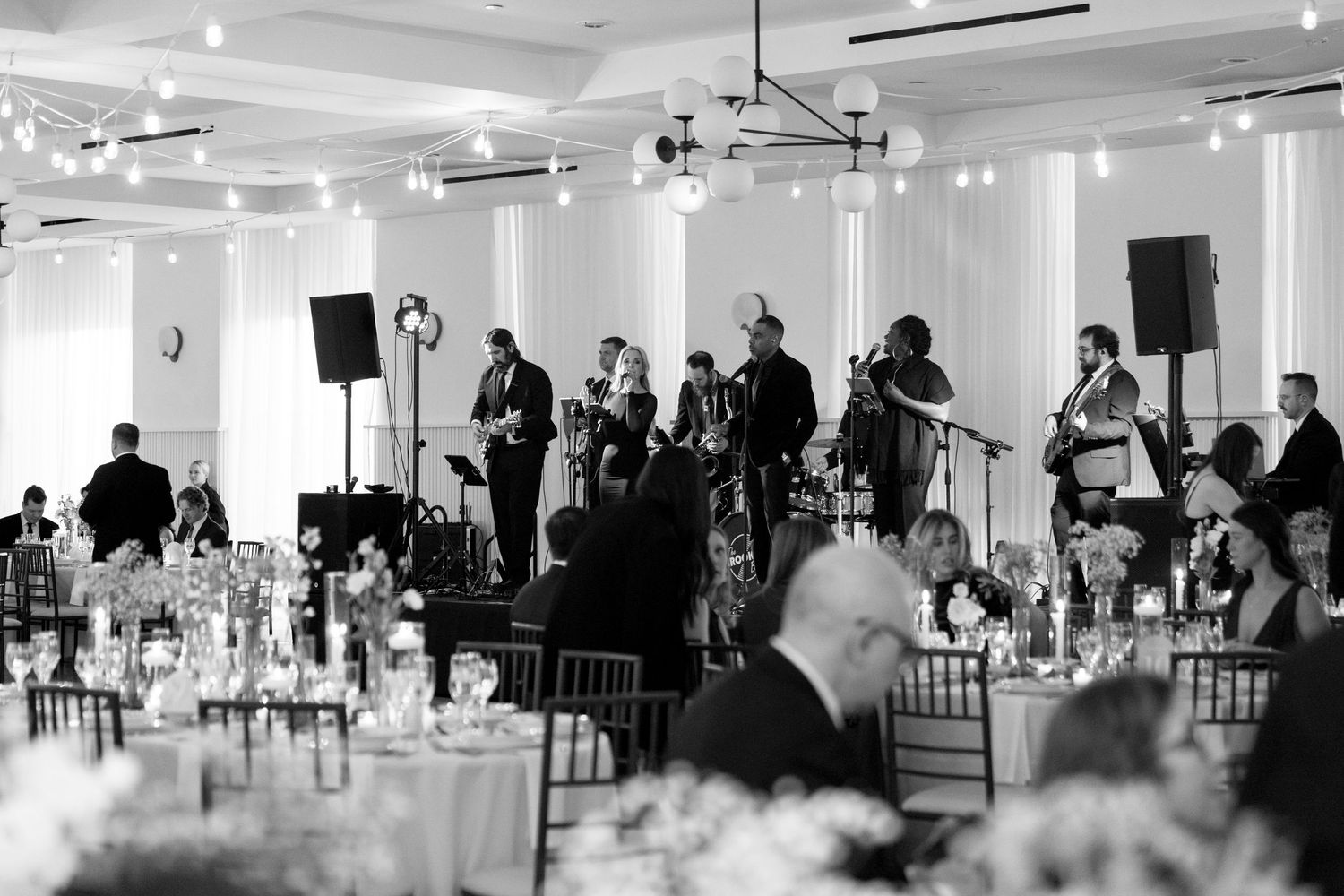 Live band performing at an elegant wedding reception in a grand ballroom with string lights and formal table settings.