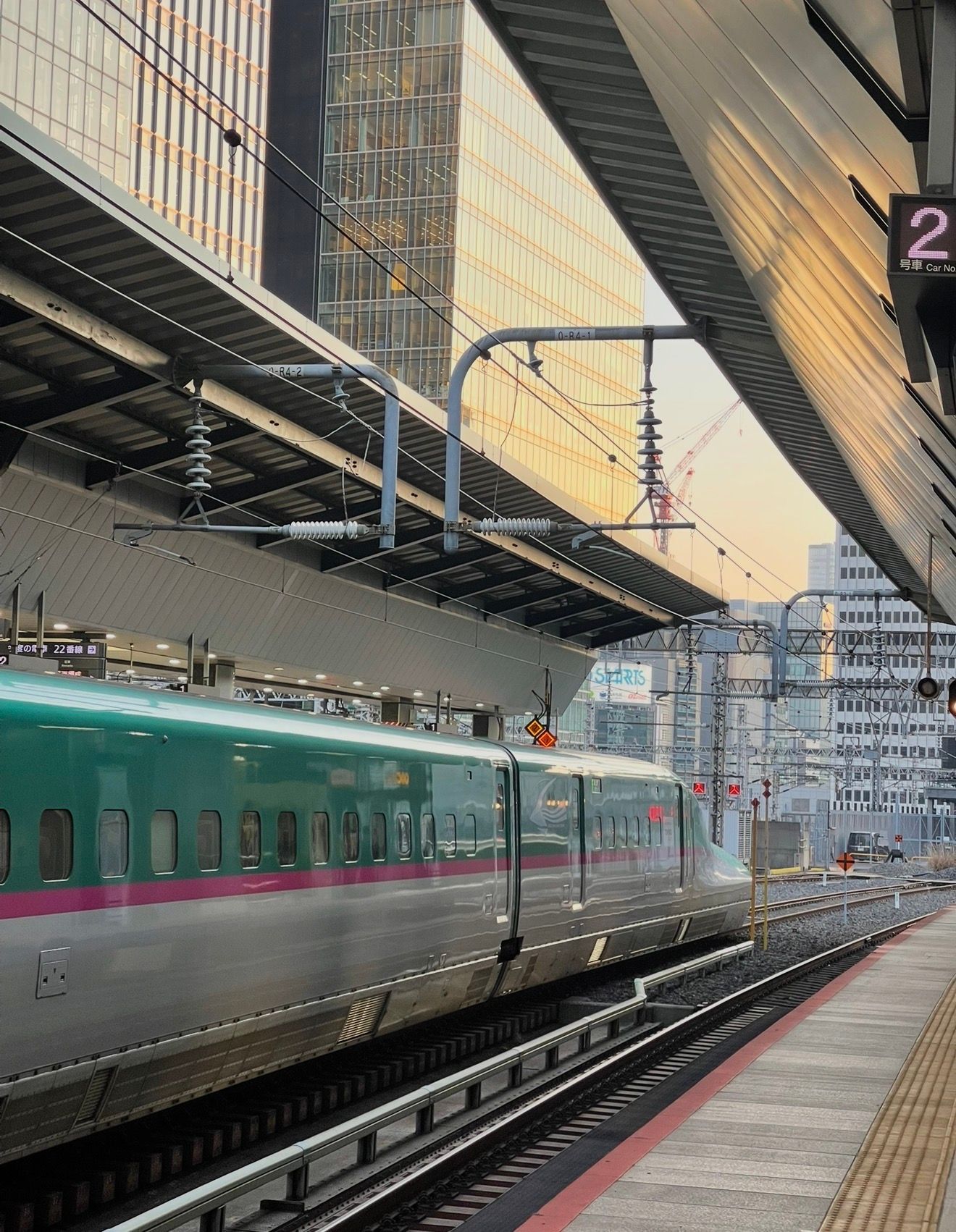Shinkansen bullet train at a Japanese station platform with modern skyscrapers in the background.