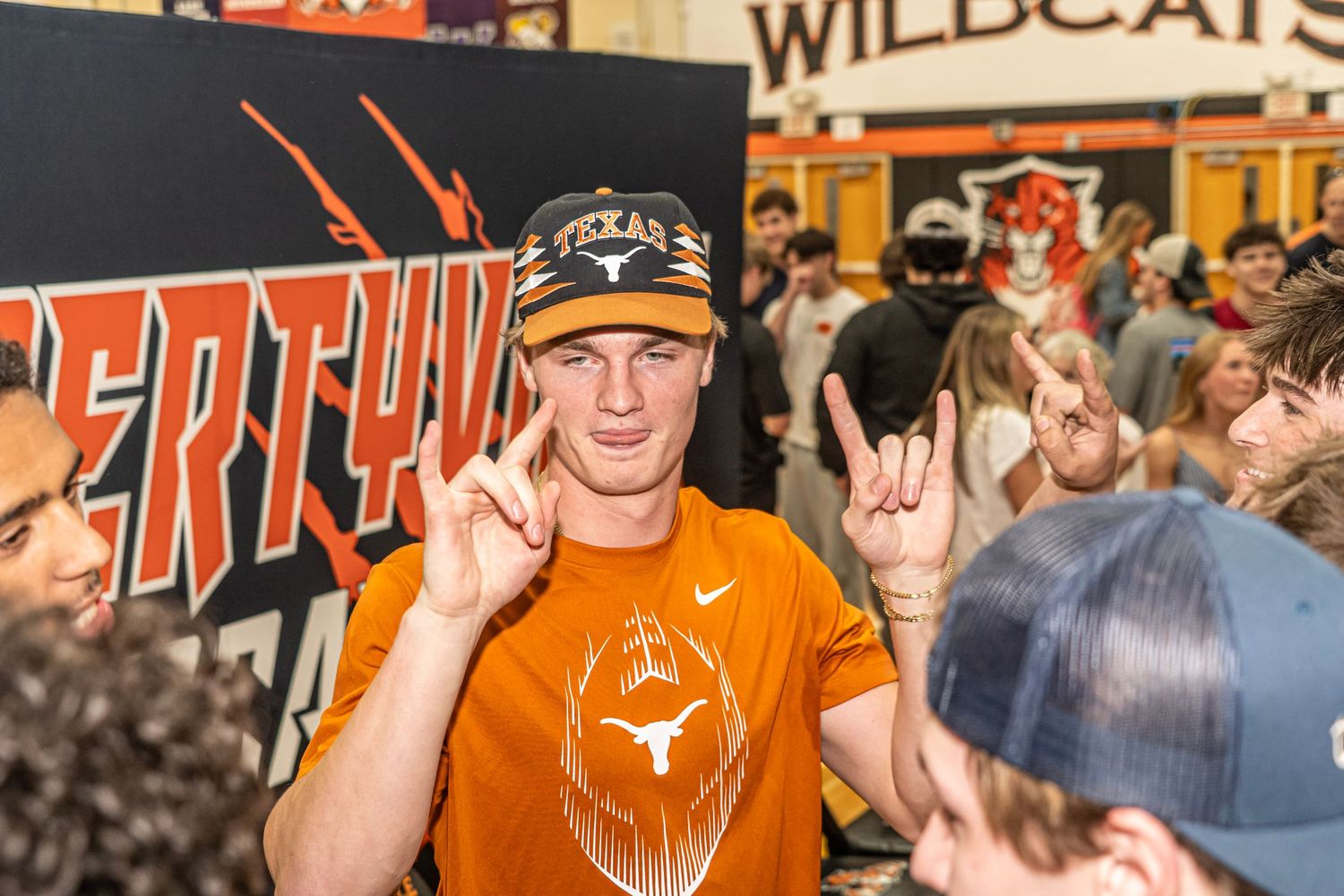 Texas Longhorns recruit signs commitment wearing orange Texas gear, flashing Longhorns hand sign at signing day event.