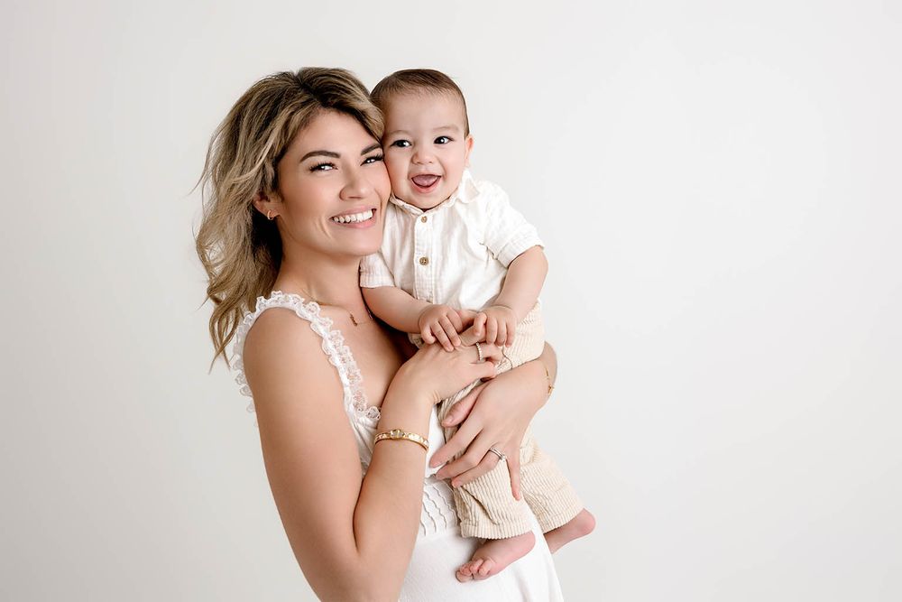 Smiling mother holding her happy baby boy in a white studio portrait.