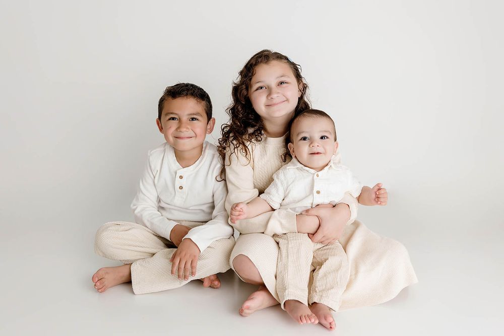 Three young siblings sitting together smiling by Temecula family photographer.