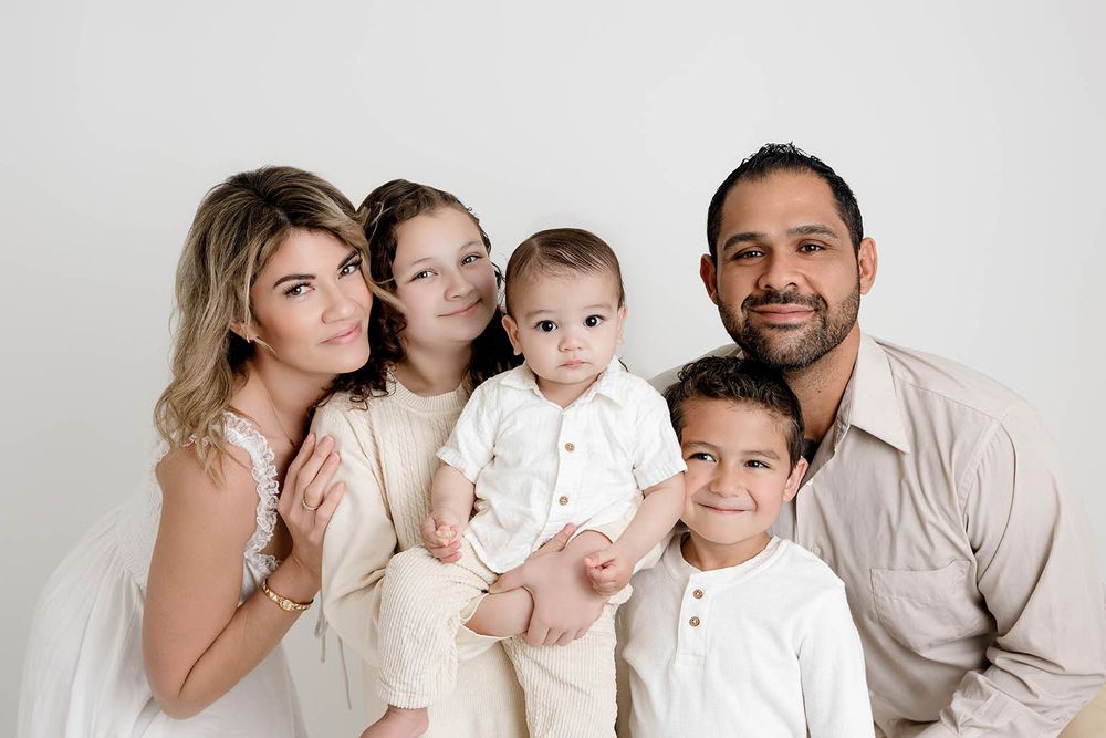 A happy family of five poses together in coordinating neutral outfits against a white background by Temecula family photographer.