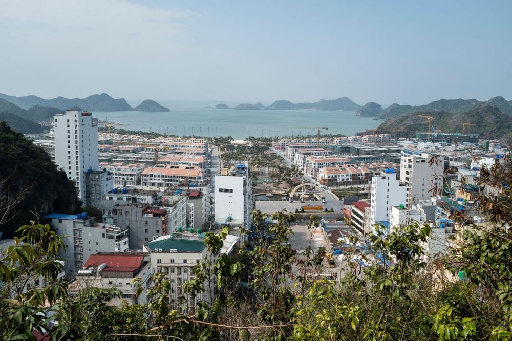 Aerial view of Cat Ba Island town with white buildings, harbor, and karst mountains in Ha Long Bay, Vietnam.