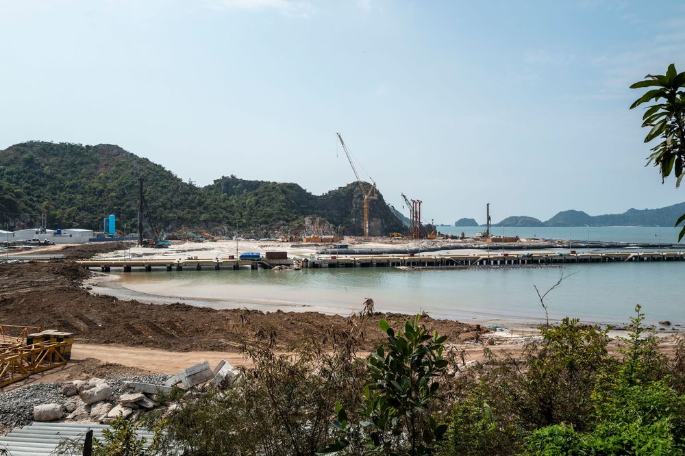 Construction of a new pier and port facility along a scenic coastal bay surrounded by green hills.
