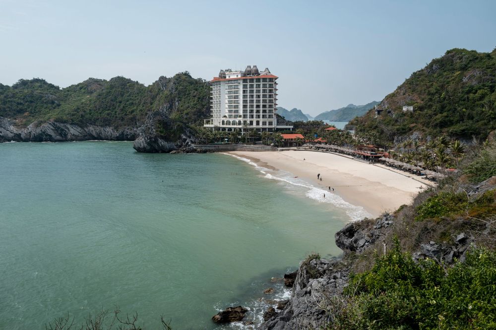 Luxury hotel overlooking a pristine sandy beach cove surrounded by rocky limestone cliffs in Vietnam.