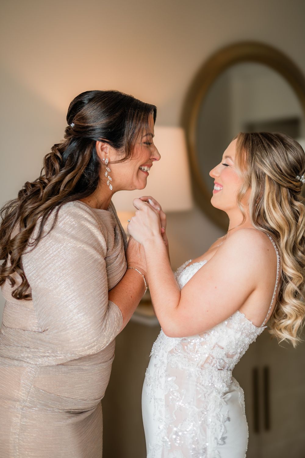 Bride and mother share a joyful moment smiling at each other during wedding day preparations.