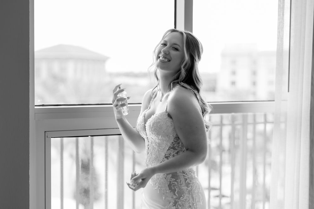 Bride in lace wedding dress applying perfume by window, black and white bridal preparation photo.