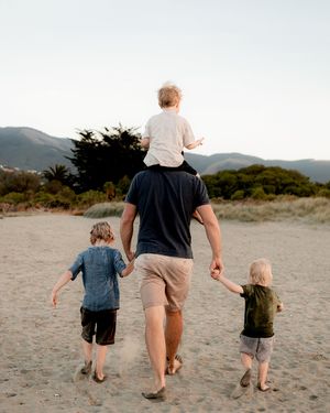 father and three sons walking together on the beach