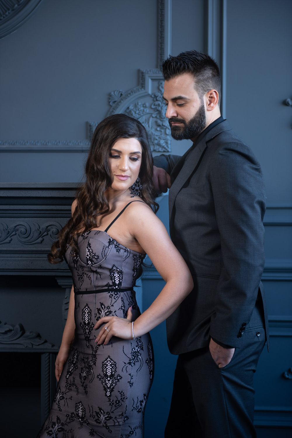 Elegant couple posing in a dark luxury interior, woman in sequined dress and man in black suit.