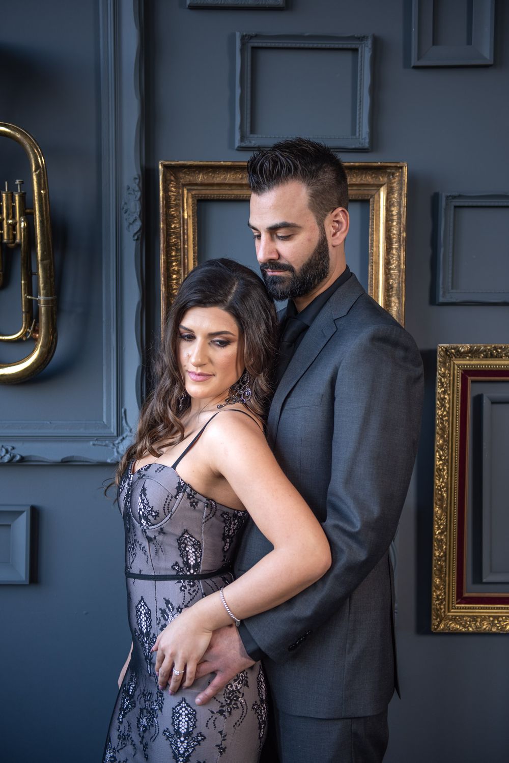 An elegant couple poses intimately in a sophisticated room with ornate gold frames.