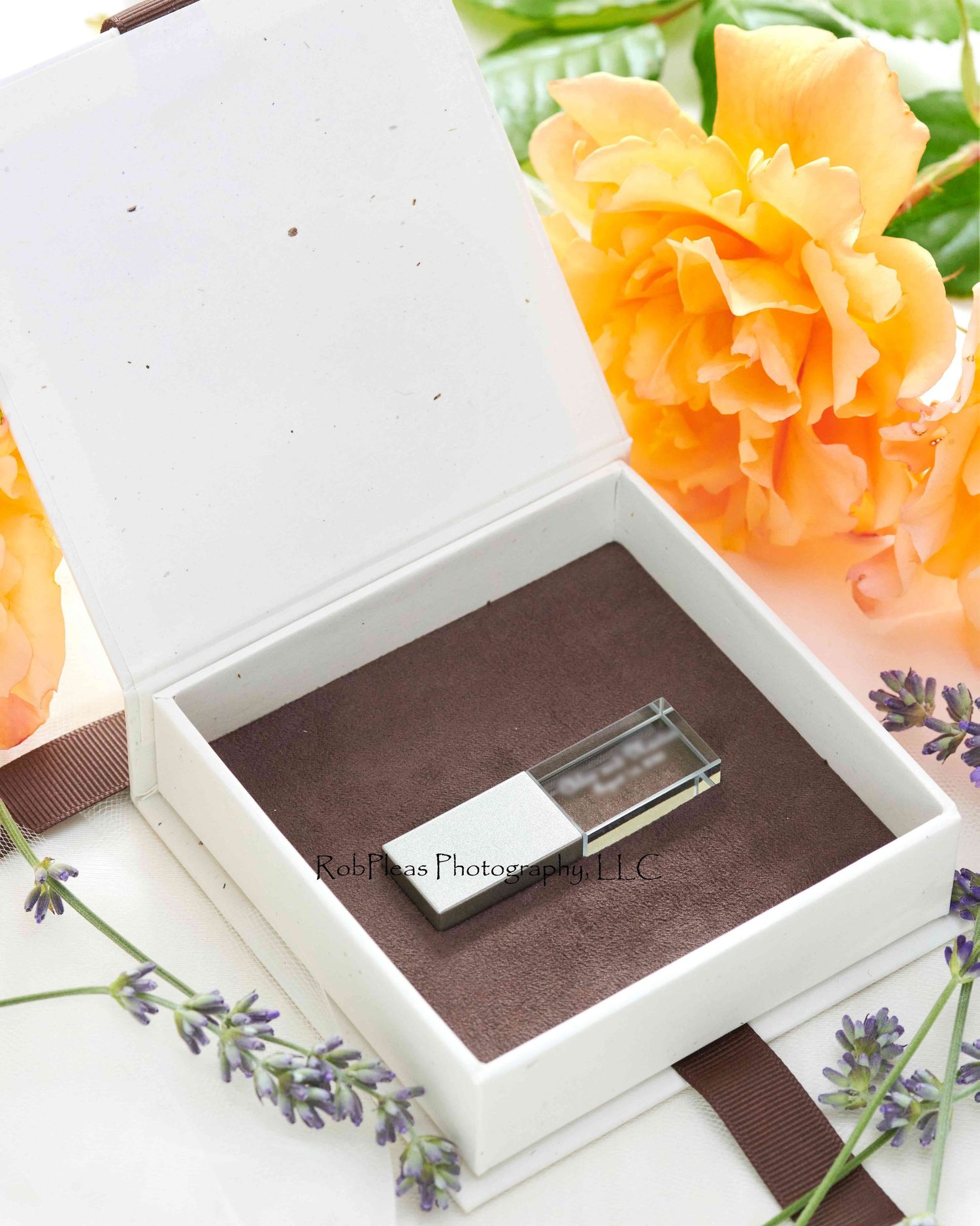 USB presentation box surrounded by lavender blossoms and orange roses.  The box is open, showing the brown interior and clear USB drive.