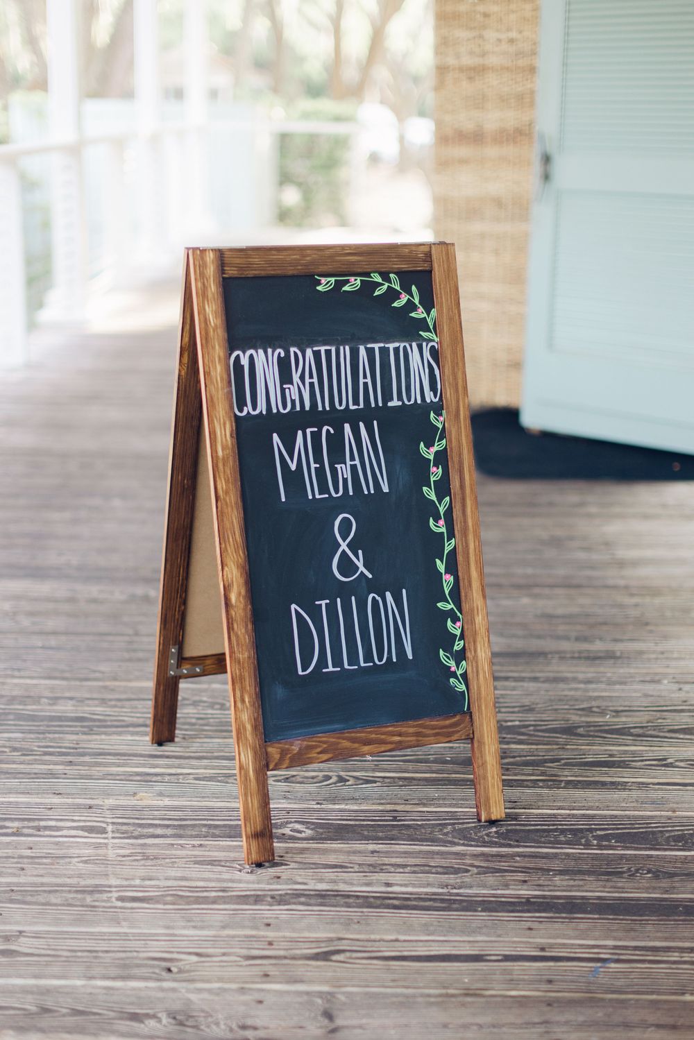 A wooden A-frame chalkboard sign reading Congratulations Megan and Dillon on a rustic outdoor deck.