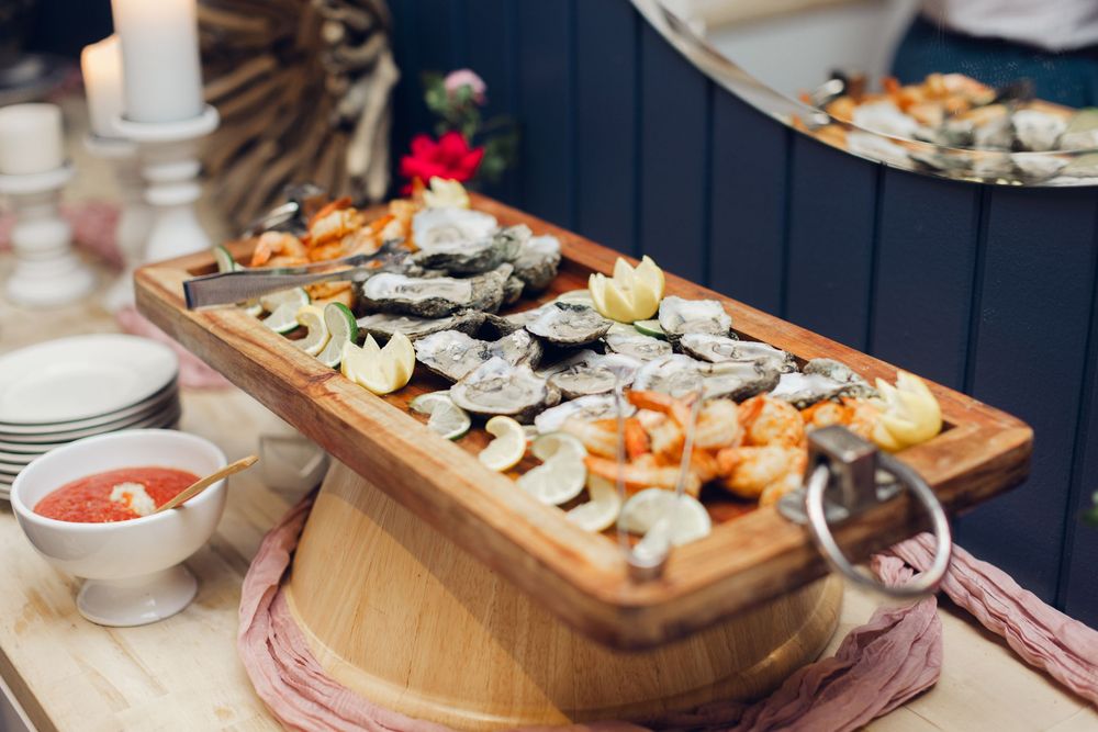 Elegant seafood platter with oysters, shrimp, and lemon on a wooden board with dipping sauce at a catered event.