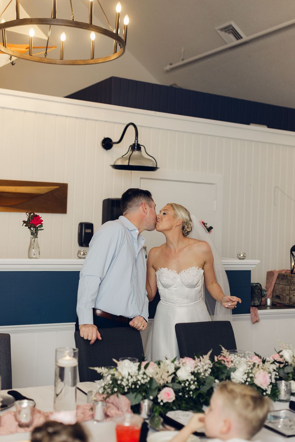 Bride and groom sharing a kiss at their wedding reception table adorned with pink floral centerpieces.
