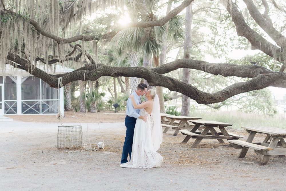 Bride and groom share a romantic kiss under a sprawling oak tree draped with Spanish moss at an outdoor wedding venue.