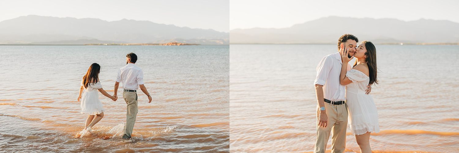 Couple holding hands wading in shallow lake water at sunset with mountains in background during romantic engagement session.