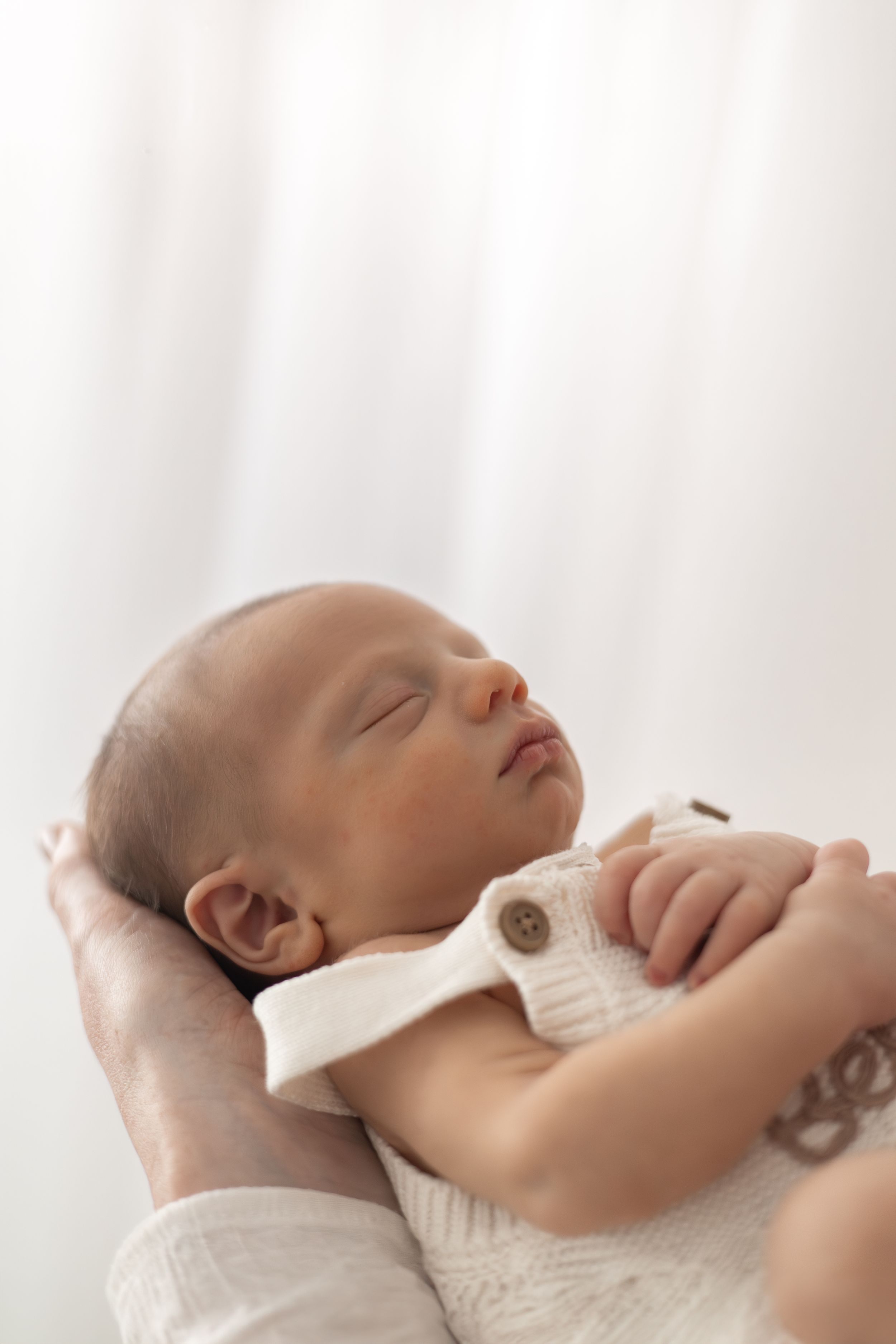 A sleeping newborn baby in a white knit outfit cradled gently in mums hands  during newborn photographer Nottingham