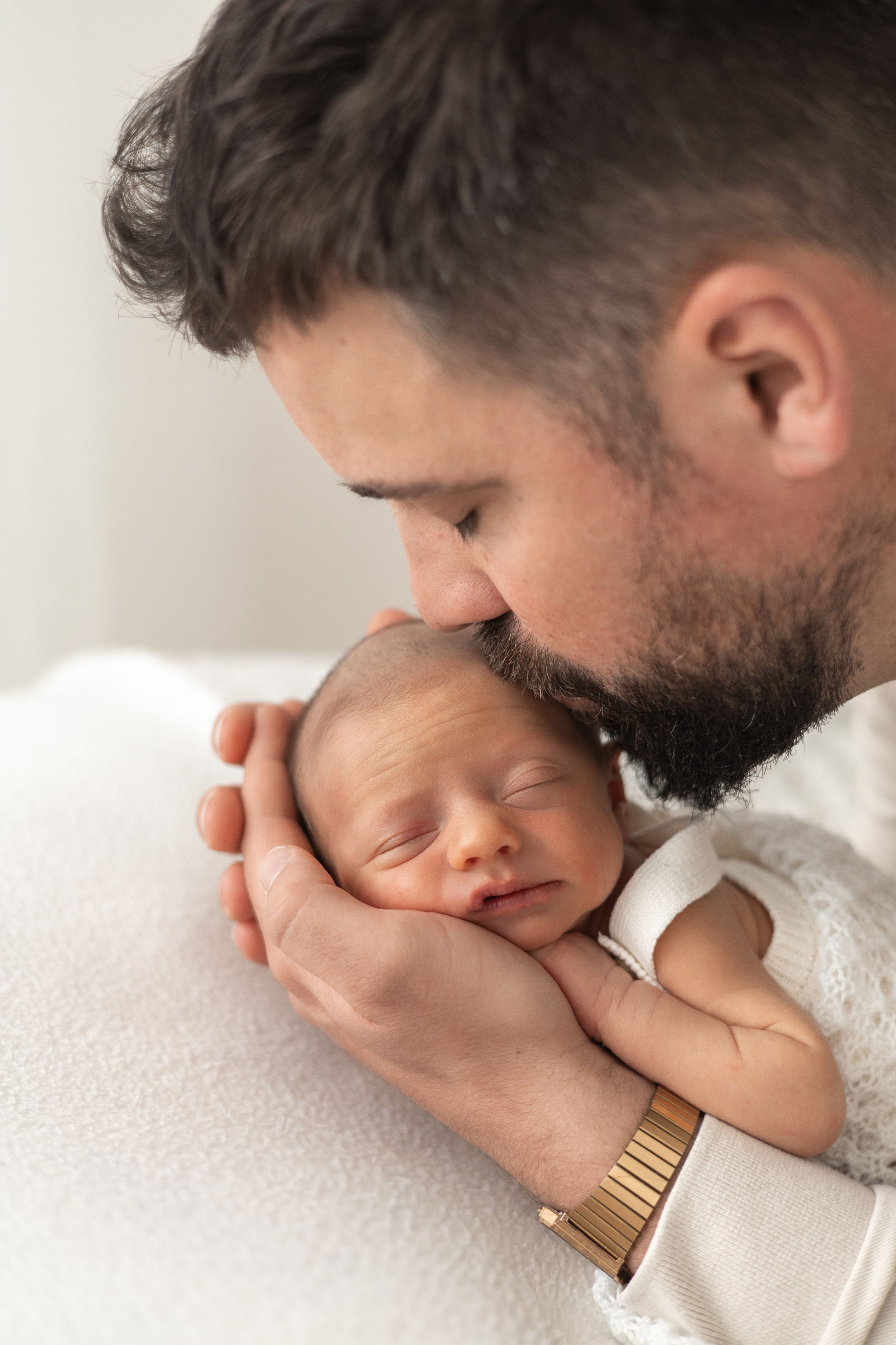Dad gently kissing his sleeping newborn baby while cradling the infant in his hands during newborn photographer Nottingham
