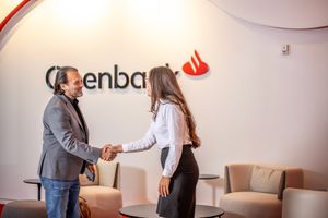 Two business professionals shake hands in an office lobby with Openbank logo on the wall.