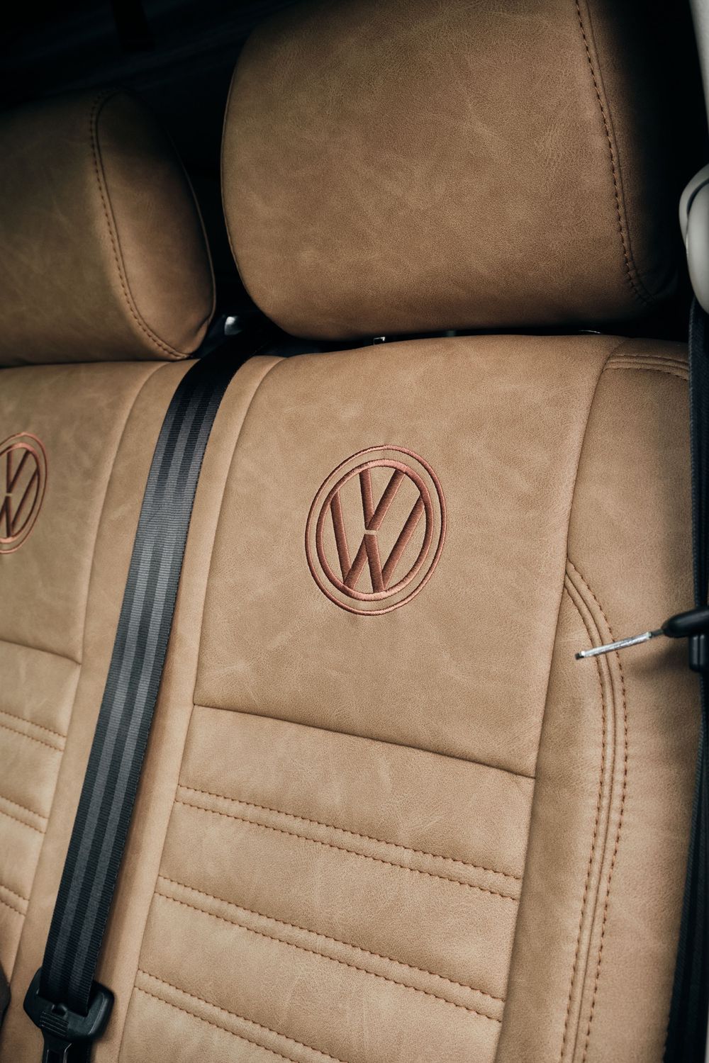 Tan leather Volkswagen car seat with embossed VW logo and black seatbelt visible in vehicle interior.