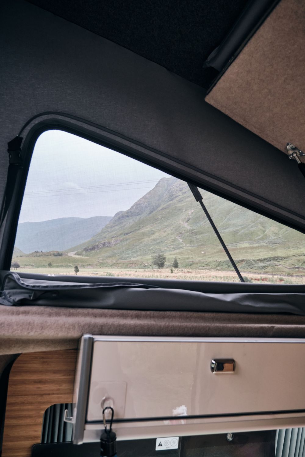 View from inside a camper van window overlooking a scenic mountain landscape with green hills.