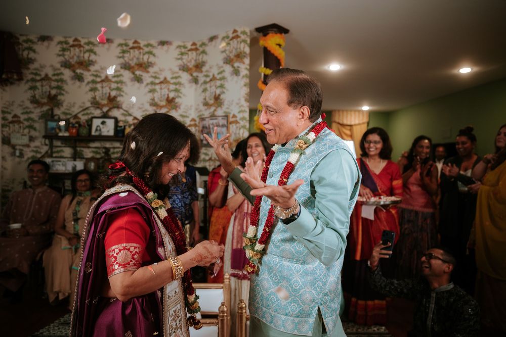 Bride and groom exchange garlands during a vibrant Indian wedding ceremony indoors with guests watching.