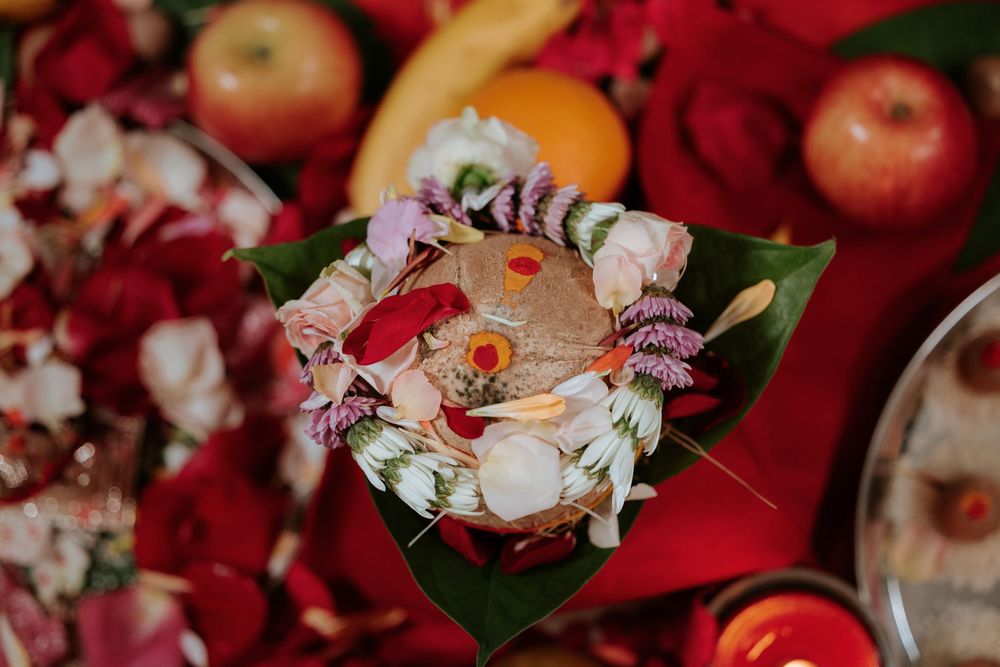 Elegant floral arrangement with roses and wildflowers on tropical leaves surrounded by fruits and red decor.