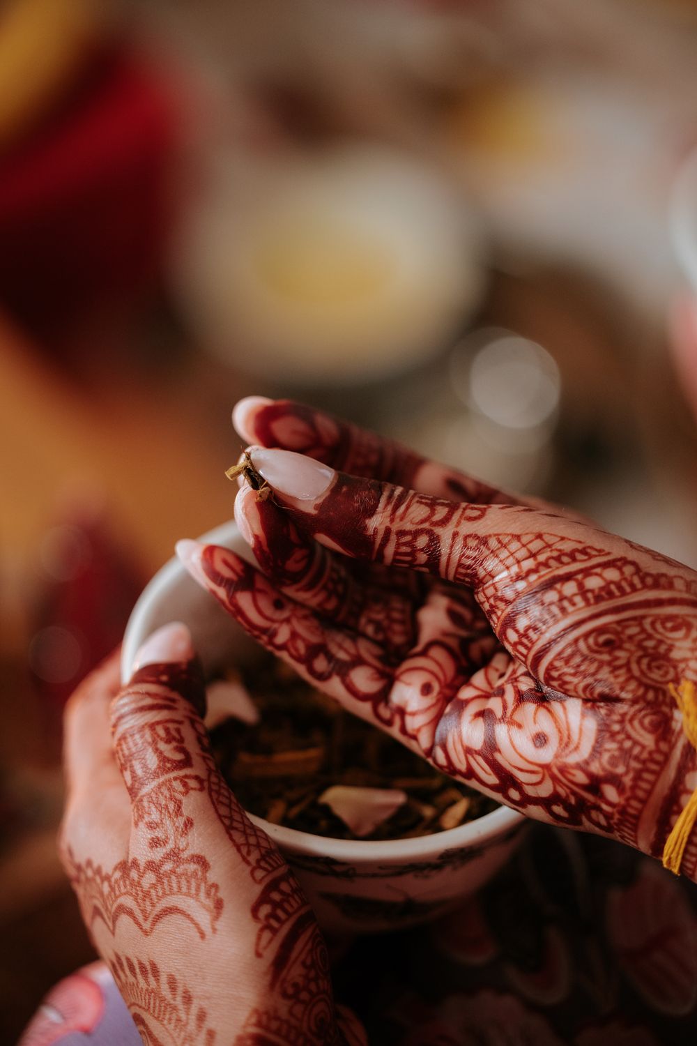 Close-up of hands adorned with intricate red mehndi henna designs holding a small white cup at an Indian wedding.