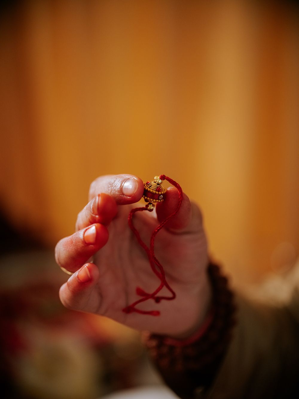 Hand holding a red rakhi thread with golden ornament during Hindu religious ceremony.