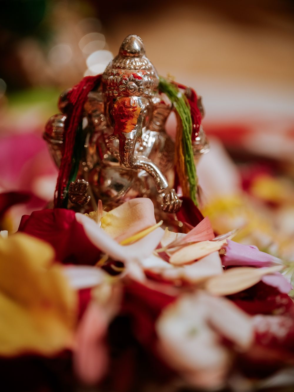 Silver Ganesha idol surrounded by colorful flower petals during a traditional Hindu wedding ceremony.