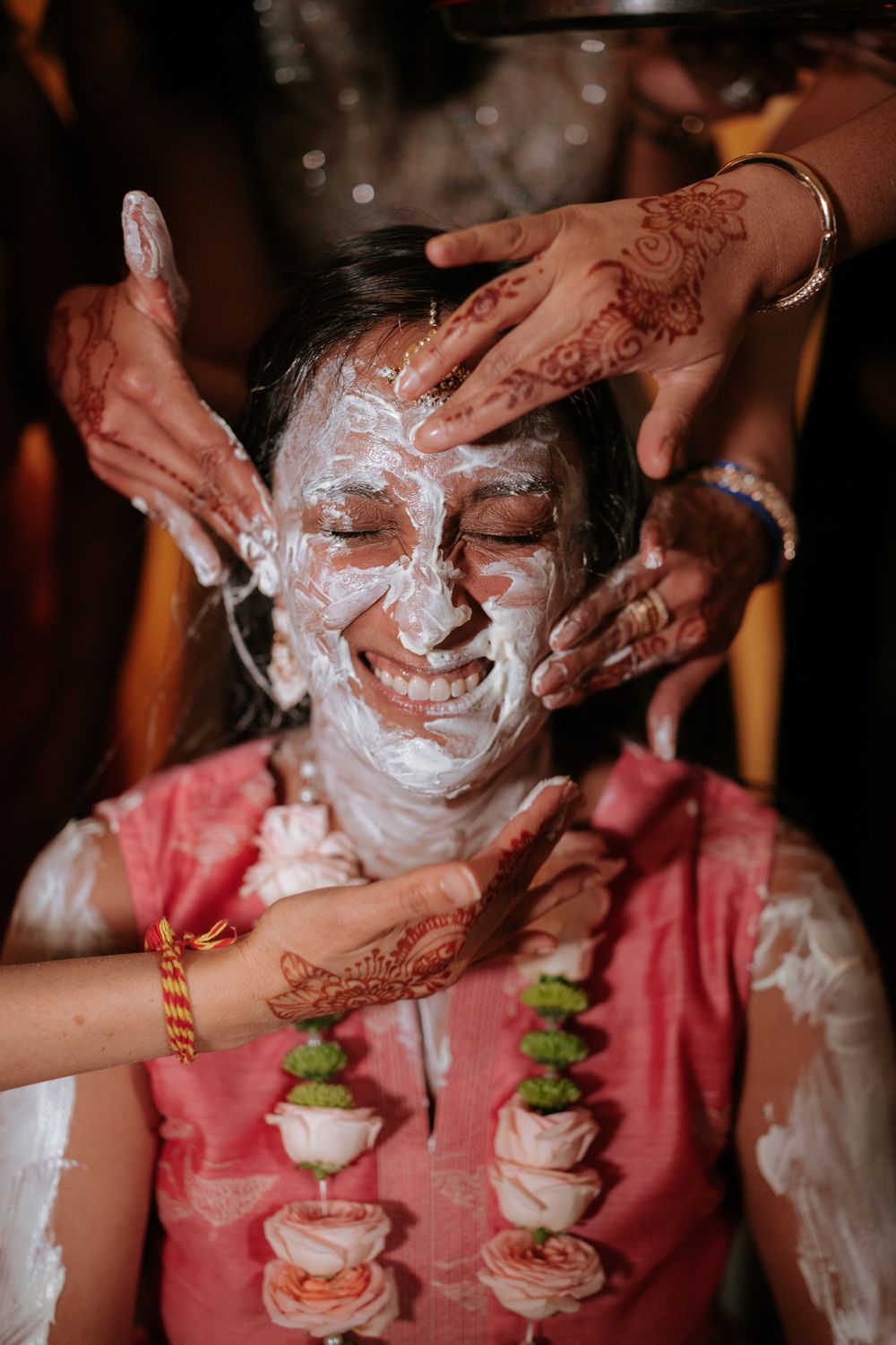 Bride smiling joyfully during a traditional Haldi ceremony with henna-adorned hands applying turmeric paste.